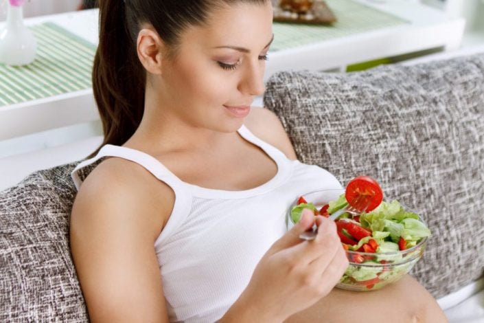 Pregnant woman holding a bowl of salad on her stomach